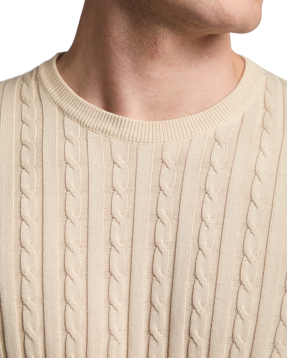 Beige cable knit sweater made from soft cotton, featuring a ribbed crew neckline and textured patterns.