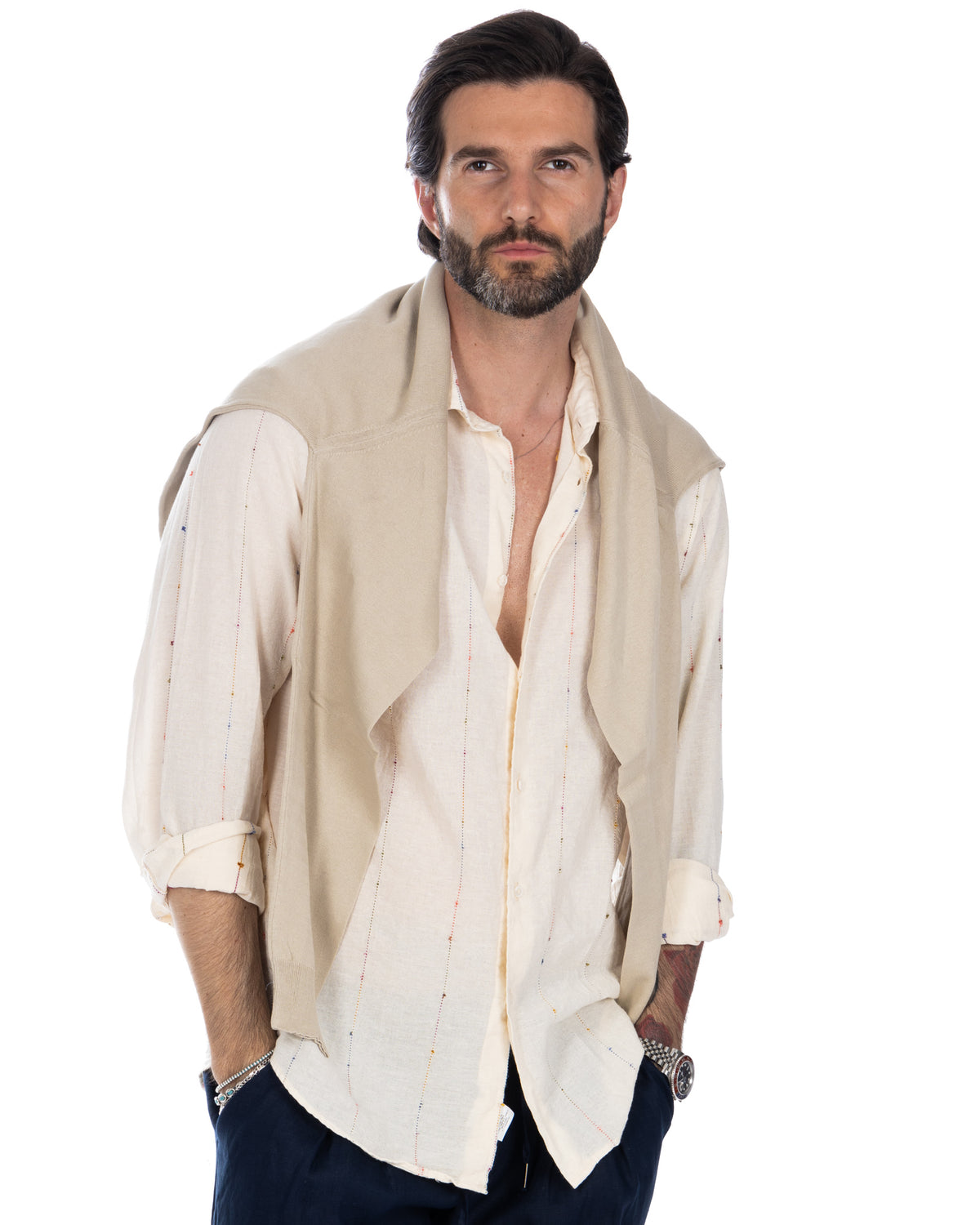 Men's cream linen button-up shirt with colorful stitching, layered under beige knit vest. Casual summer style.
