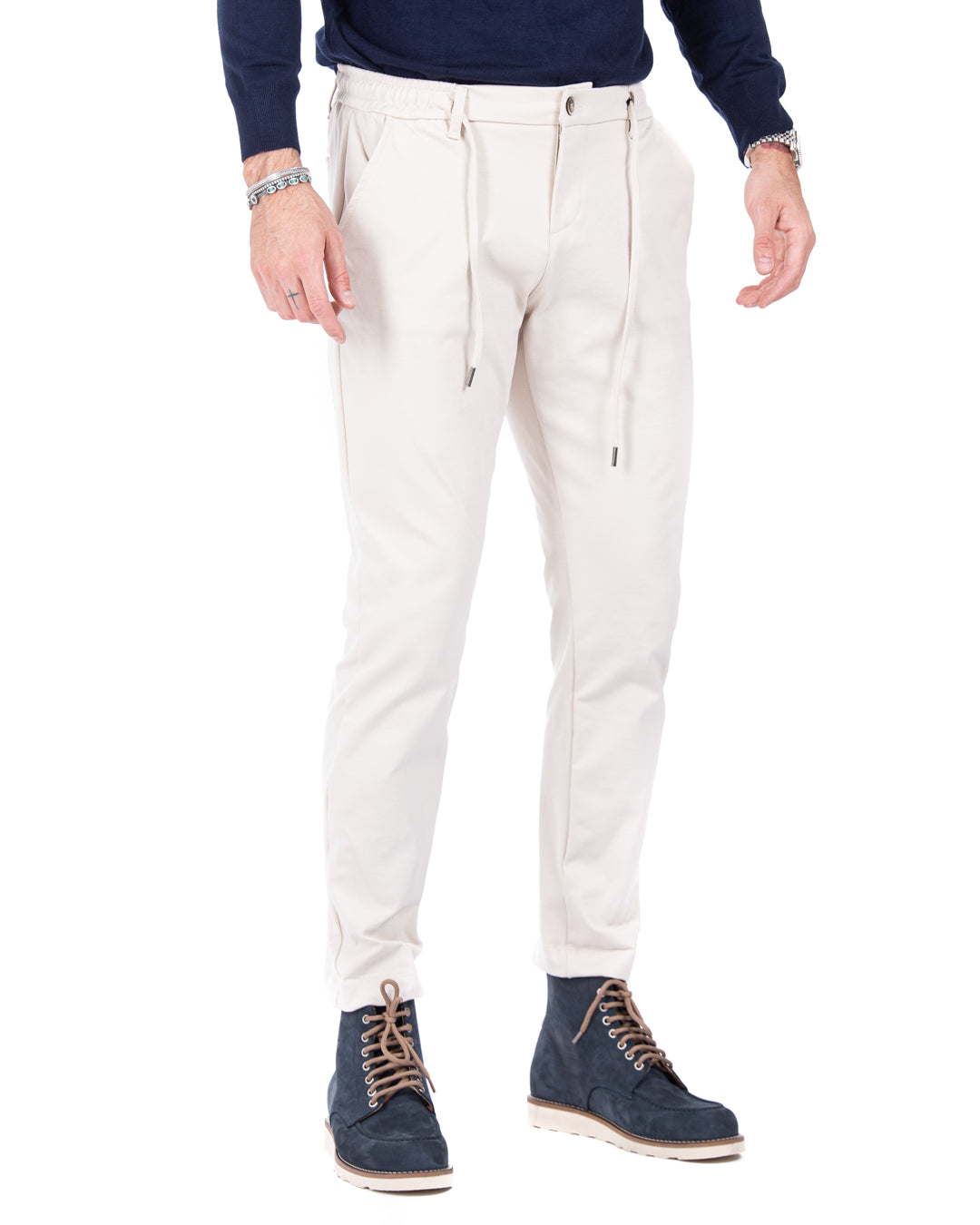 Men's cream jogger pants in soft cotton blend, featuring an elastic waistband and tapered fit, paired with navy boots.