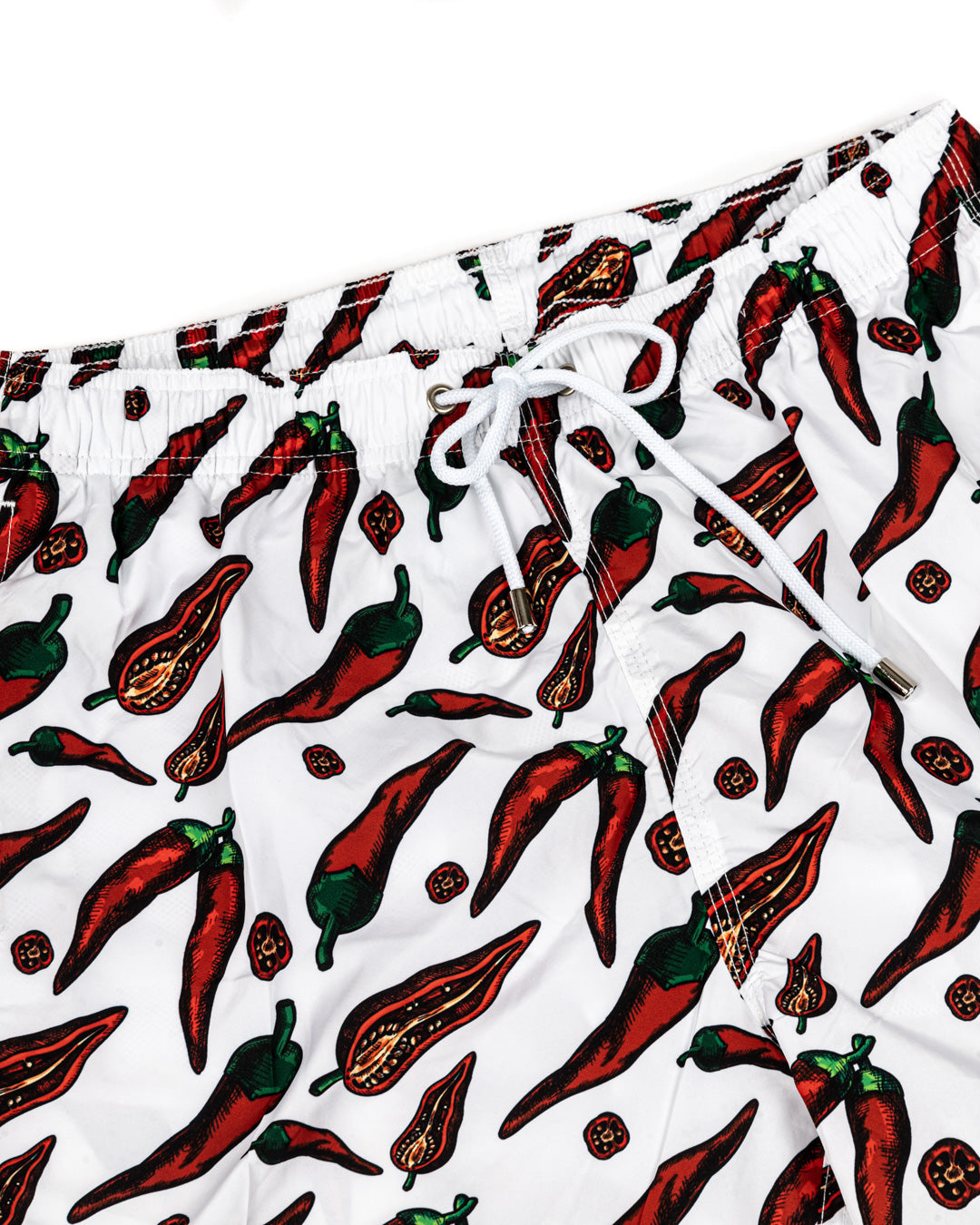 White swim trunks with red chili pepper print, elastic waist, drawstring closure. Quick-dry beach shorts.