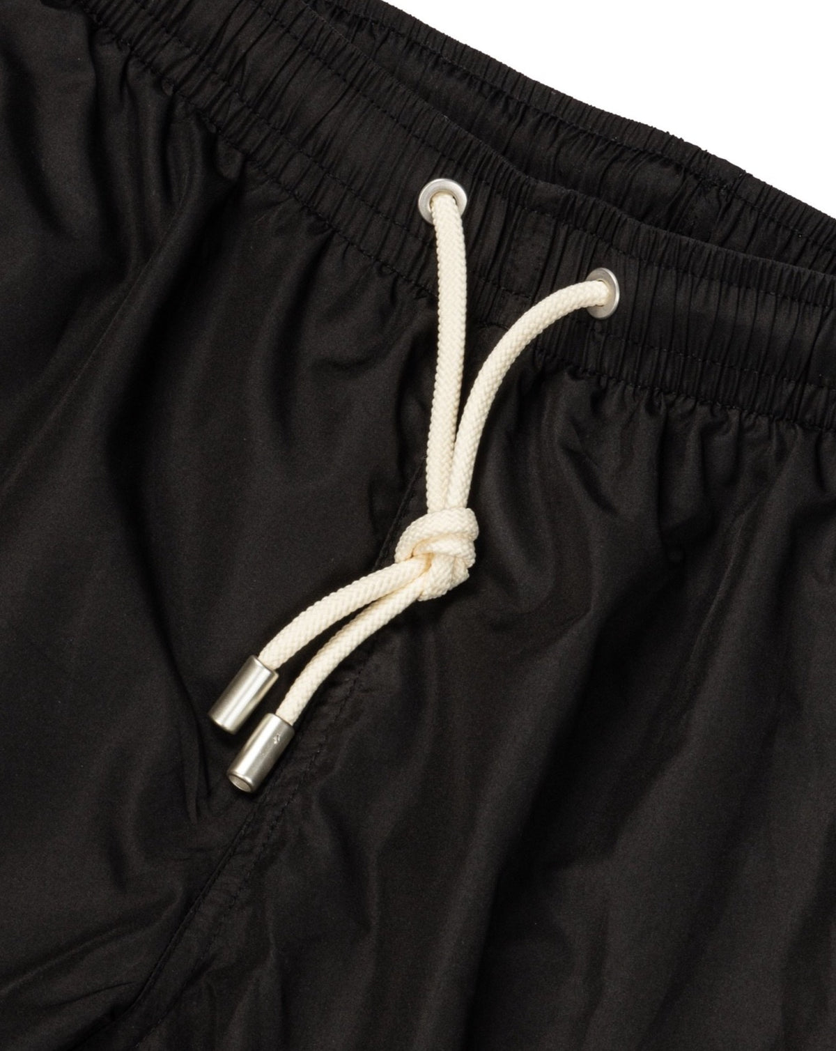 Close-up detail of black swim shorts with cream drawstring tied at the elastic waistband