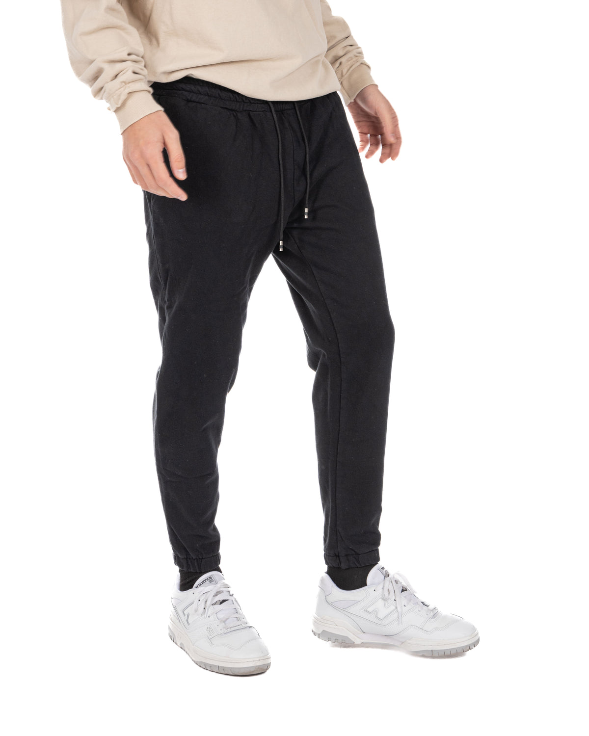 Men's black cotton drawstring jogger pants with tapered leg, worn with a beige top and white sneakers, front view