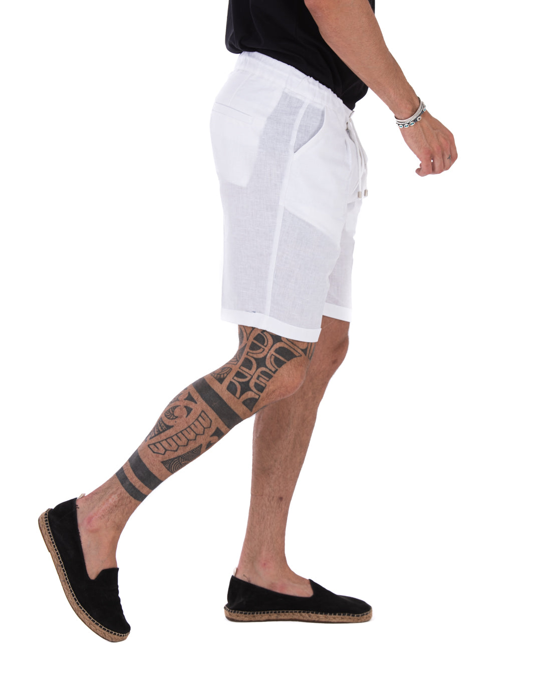 Men's white linen drawstring bermuda shorts with rolled cuffs and slant pockets, shown in side view on a model