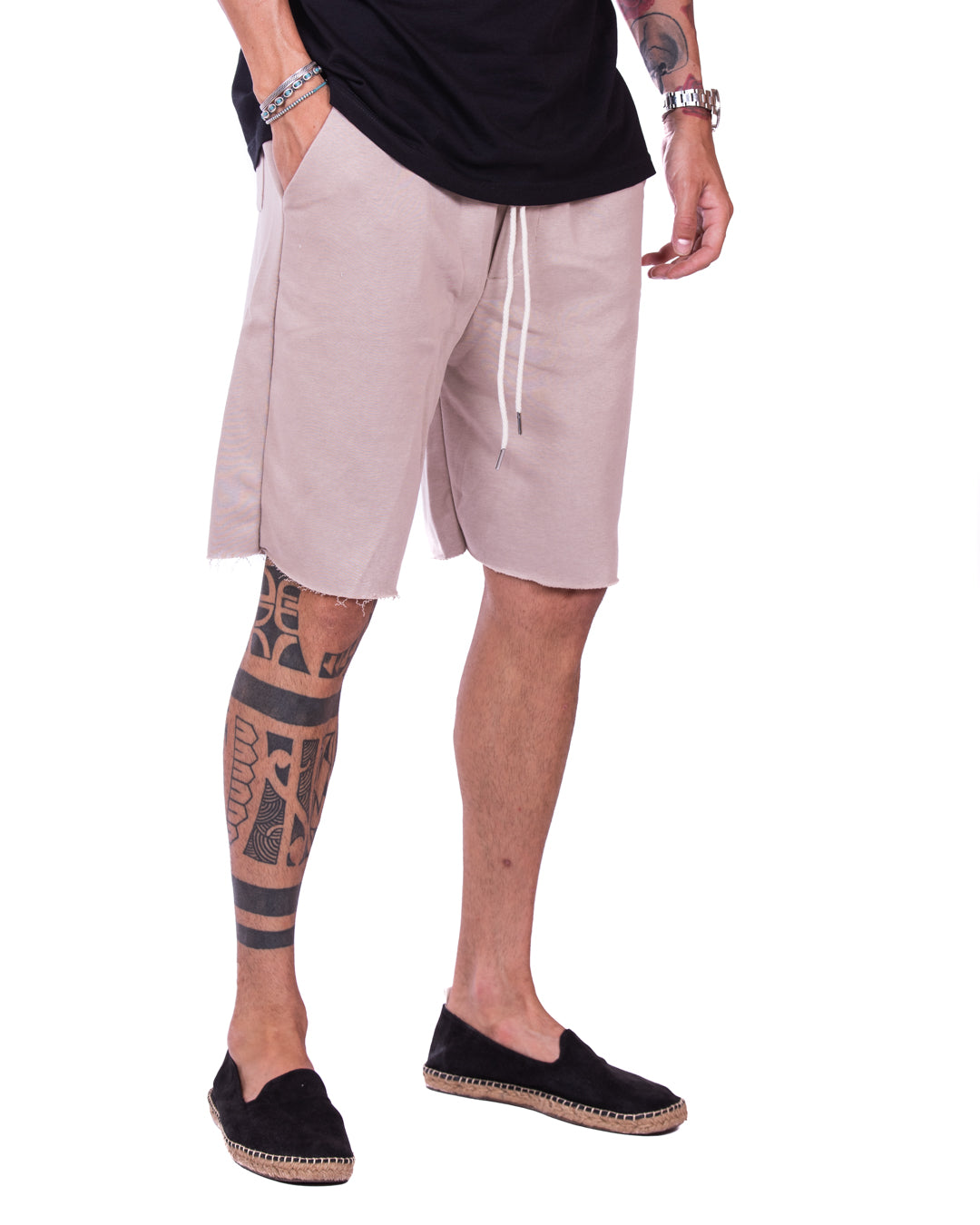 Men's beige cut-off sweat shorts with drawstring waistband and raw frayed hem, styled with black espadrilles