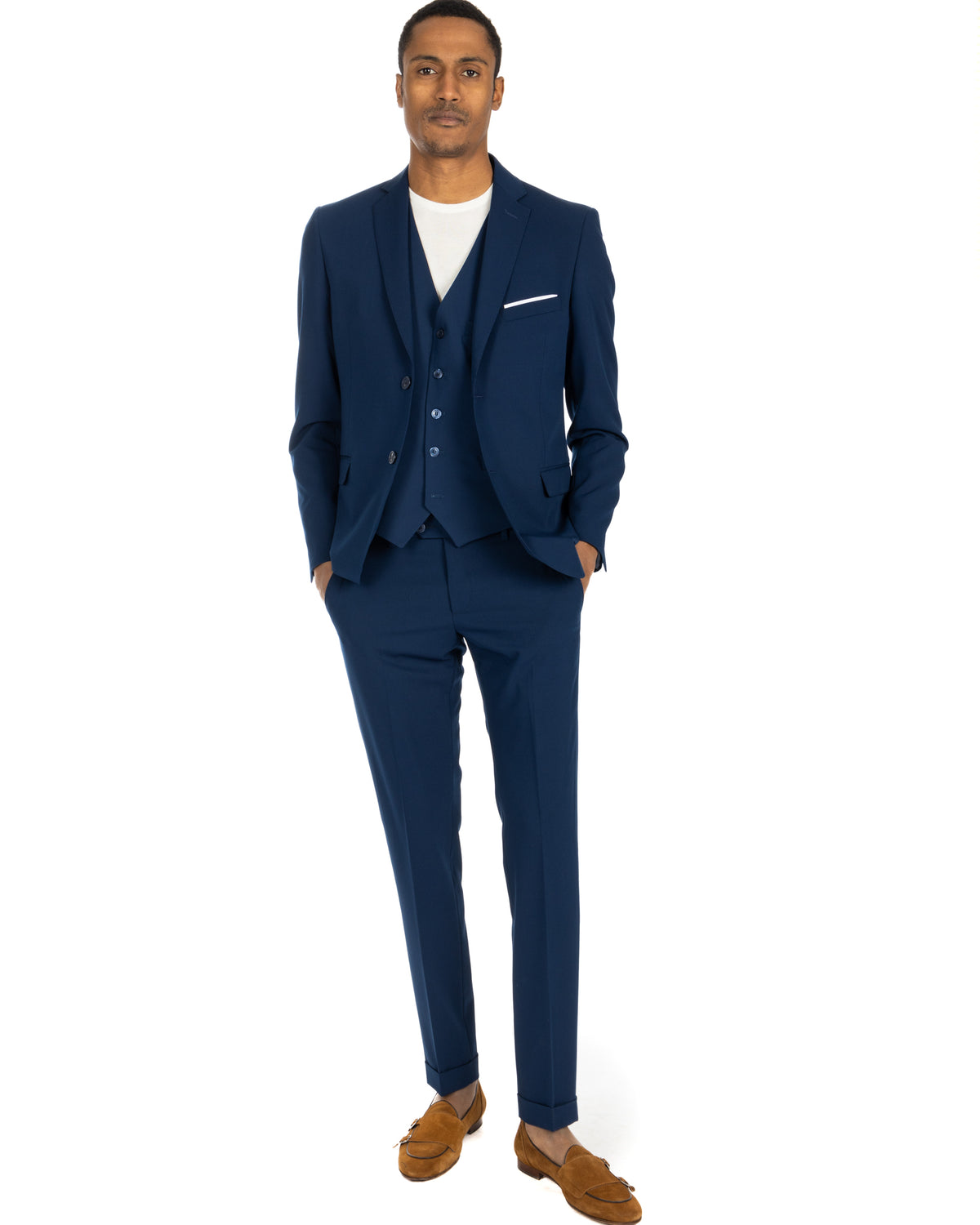 Navy blue three-piece suit with white pocket trim, paired with white t-shirt and tan suede loafers. Slim fit formal menswear.