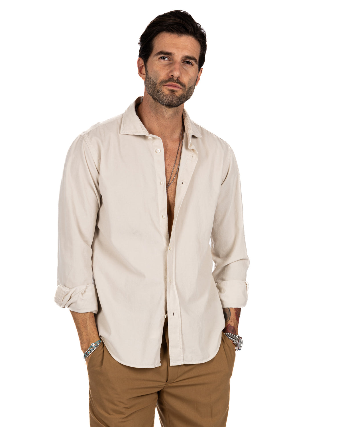 Men's cream linen button-down shirt with rolled sleeves, paired with tan trousers and silver accessories.