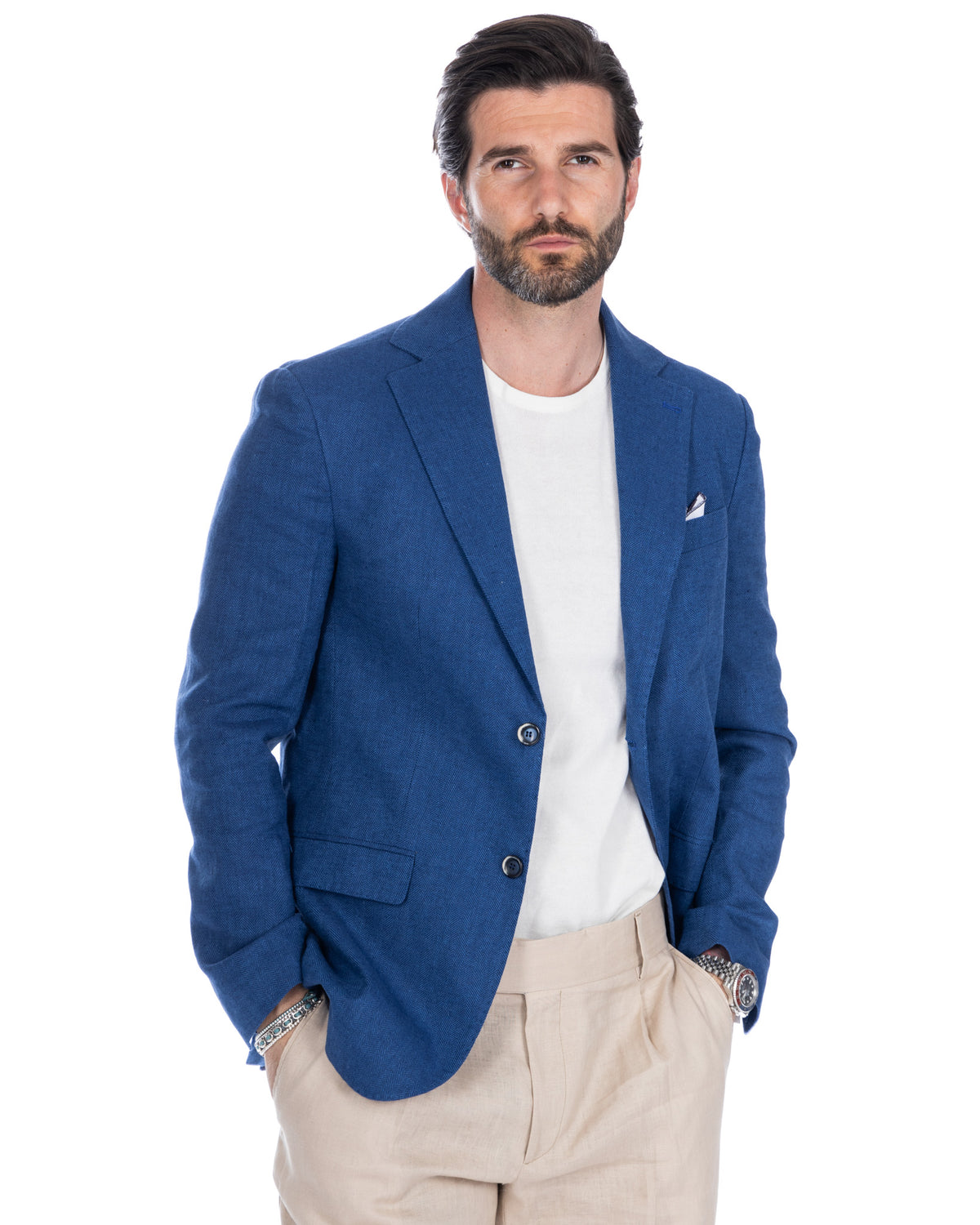 Men's blue herringbone wool blazer with white pocket square, paired with beige trousers and white t-shirt.