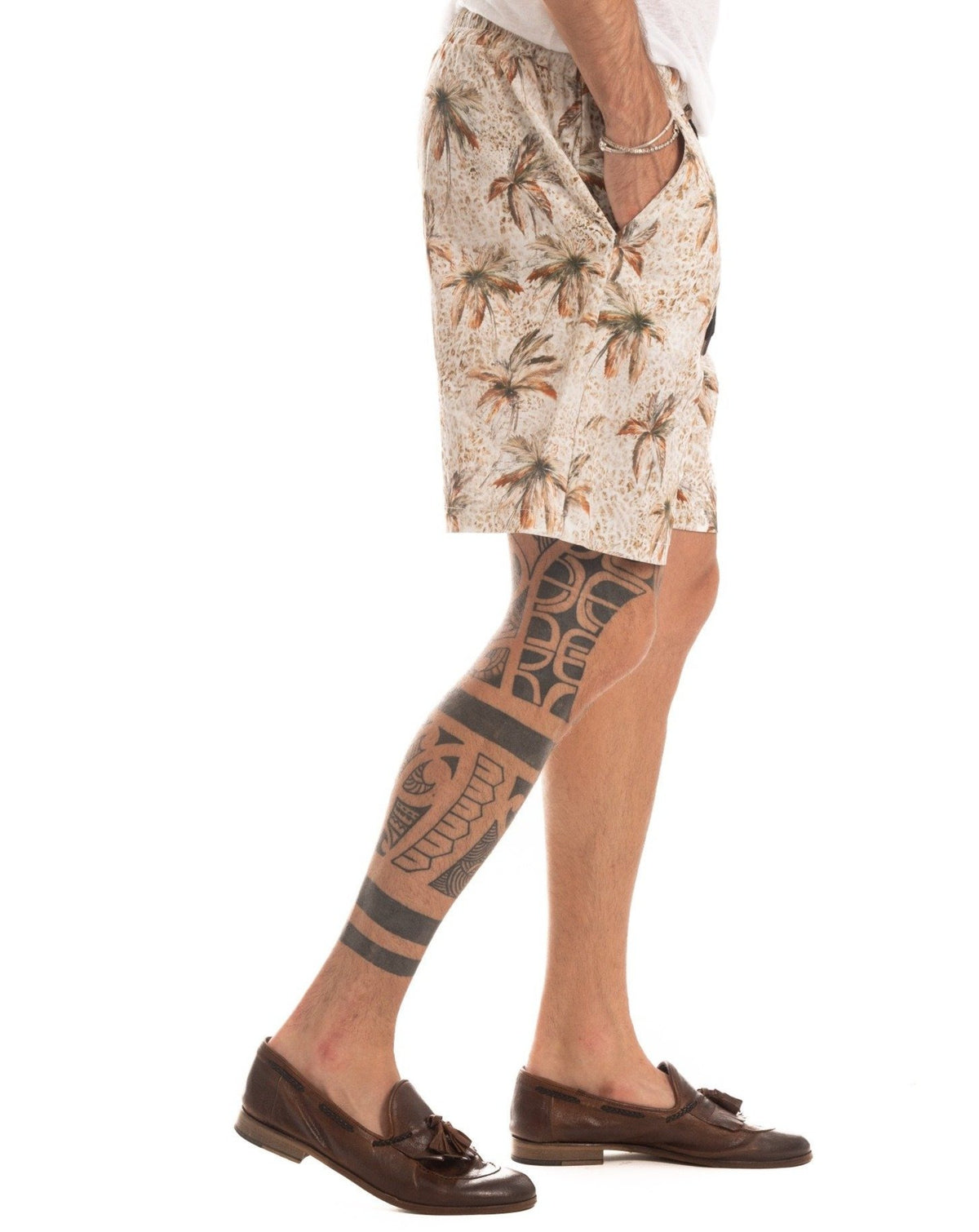 Beige palm tree print shorts shown in side profile with rolled hems