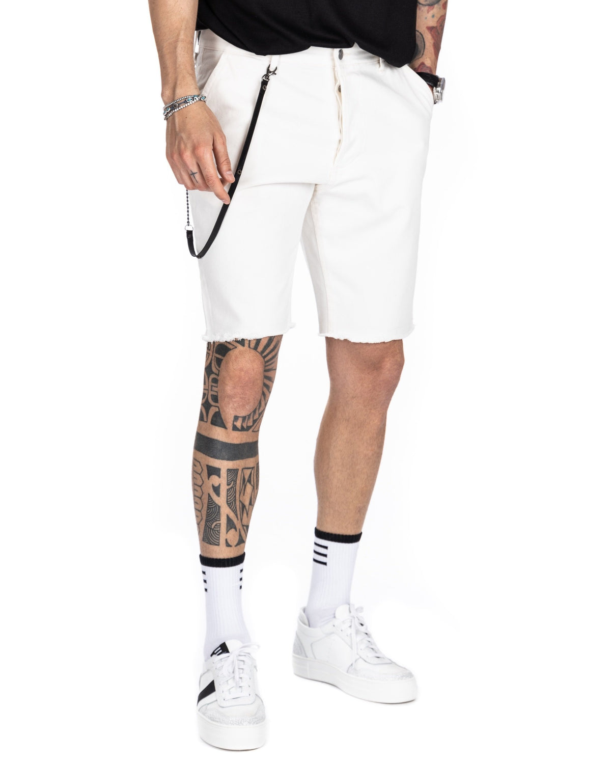 Three-quarter view of men's off-white denim Bermuda shorts with frayed hem and black leather strap detail, shown on a model