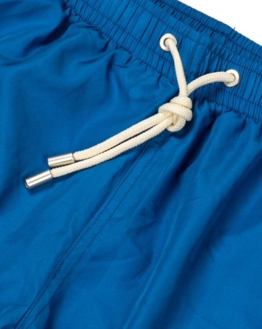 Close-up detail of blue swim shorts with cream drawstring and metal-tipped aglets