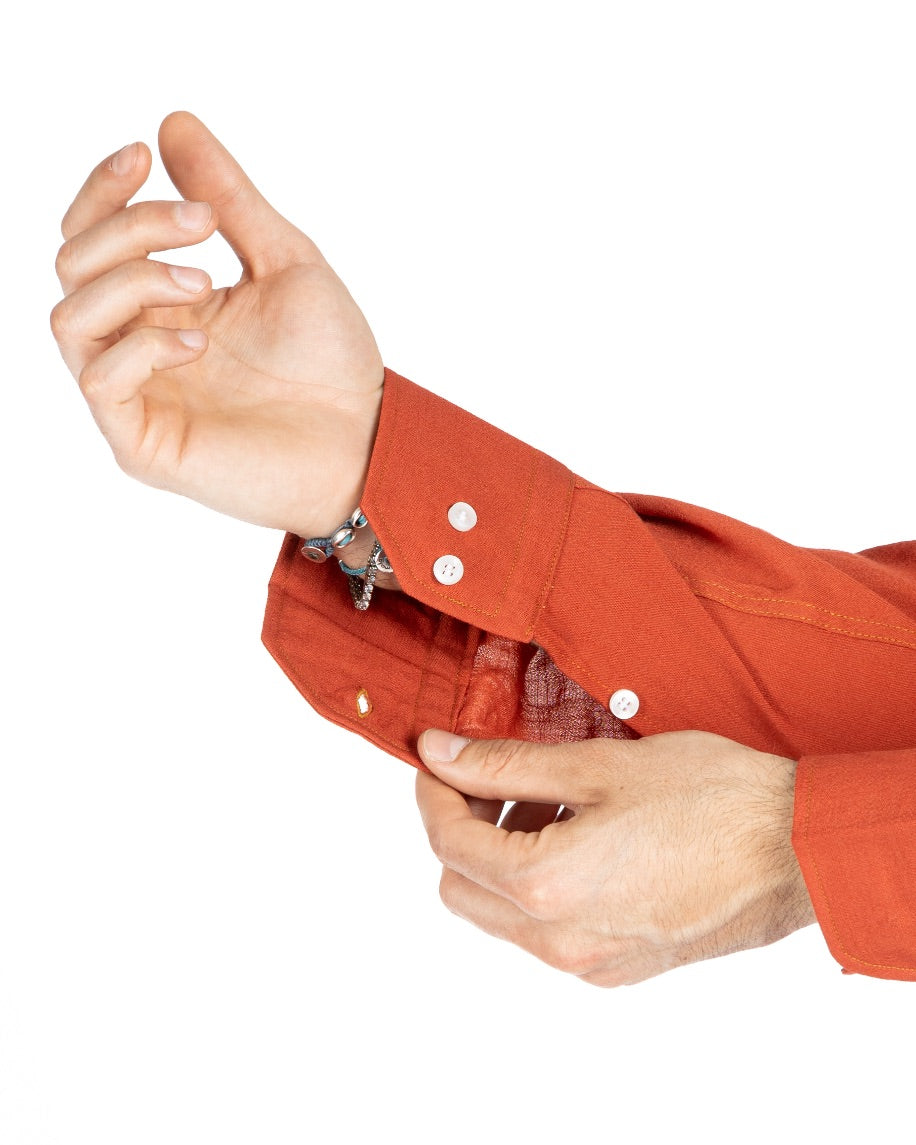 Close-up of a rust orange linen shirt cuff with white buttons, adjusted by the model's hand