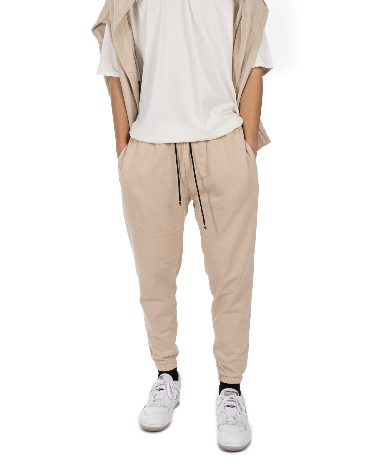 Men's beige cotton drawstring jogger pants with elastic cuffs, worn with a white t-shirt and white sneakers, front view