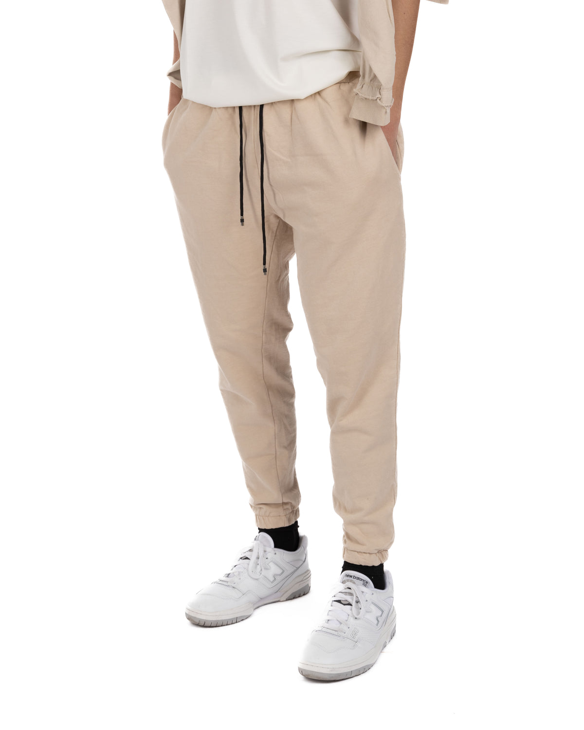 Side view of men's beige cotton drawstring jogger pants worn with a white t-shirt and white sneakers