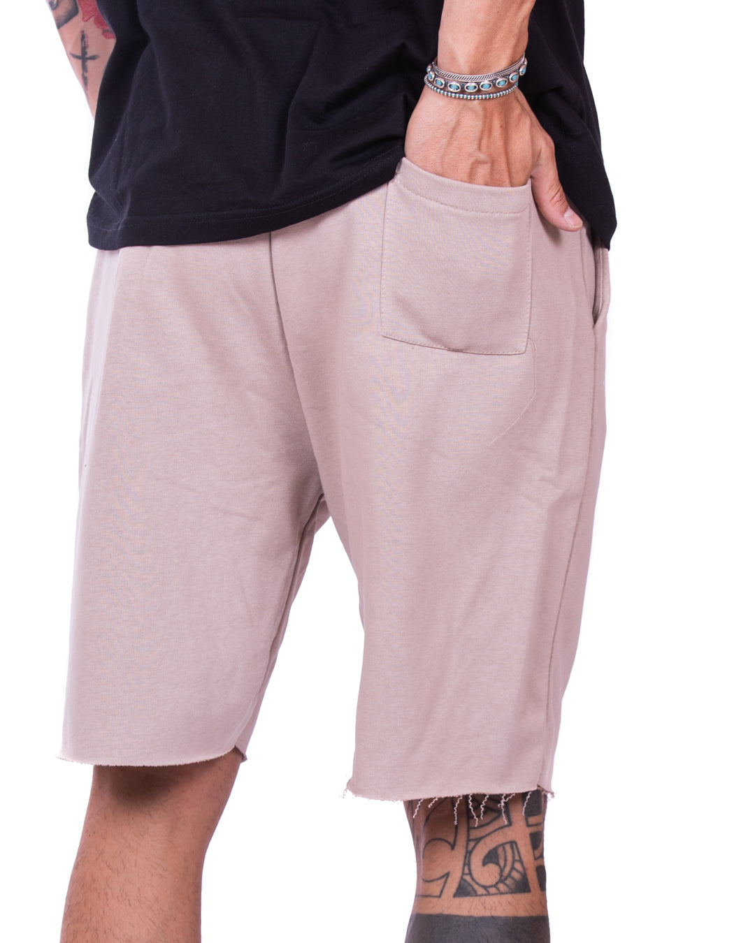 Close-up detail of beige cut-off sweat shorts with back patch pocket, shown from behind on a model
